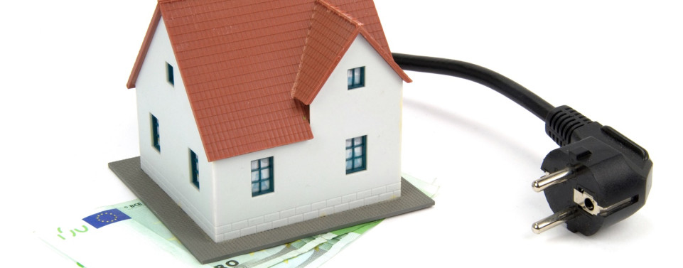 Ein Modellhaus, dass auf zwei 100-Euro-Scheinen steht und ein Stromkabel, dass aus dem Haus kommt.