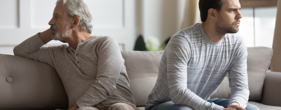 Vater und Sohn sitzen auf Sofa und sehen wütend aus. Sehen sich nicht an.