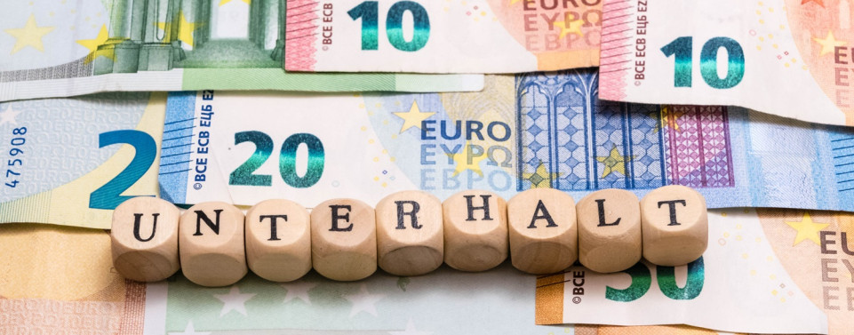 Geldscheine auf denen Holzwürfel liegen. Auf den Würfeln steht Buchstabe für Buchstabe "Unterhalt"