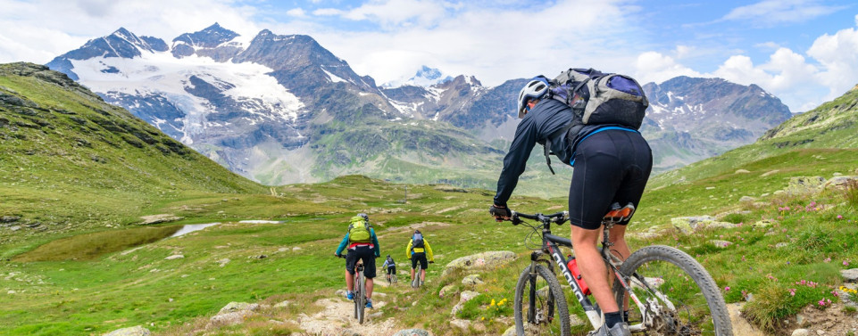 Gruppe von Mountainbiker fahren in einen unebenen Pfad in einer Berglandschaft hinunter.