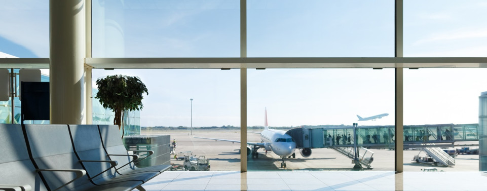 Sicht aus einem Flughafenfenster auf das Rollfeld, wo ein Flugzeug steht und Passagiere einsteigen.