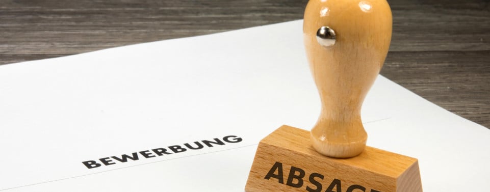 Dokument mit der Aufschrift "Bewerbung". Auf dem Dokument steht ein Holzstempel mit der Aufschrift "Absage"