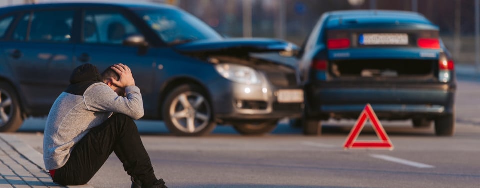 Autounfall und Mann sitzt am Straßenrand