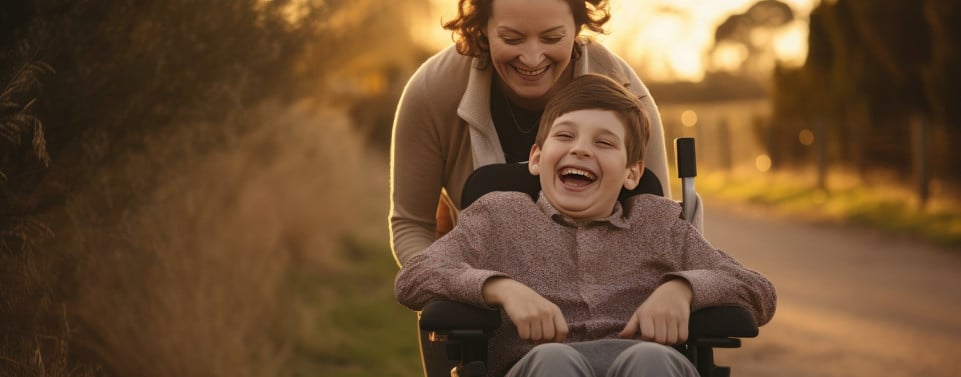 Kind mit Behinderung im Rollstuhl lacht mit Frau.