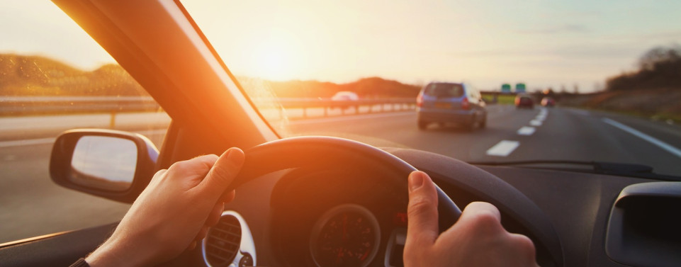 Hände am Steuer eines Autos auf der Straße im Sonnenuntergang. 