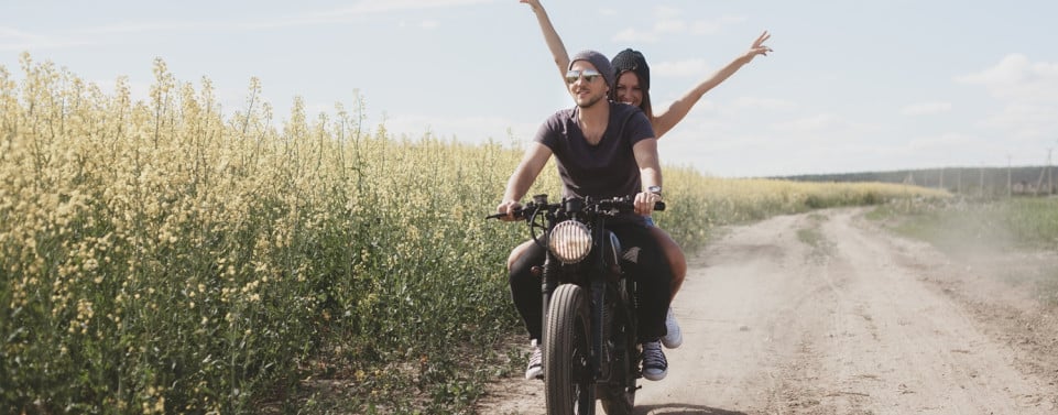 Lachendes Paar auf dem Motorrad auf Feldweg.