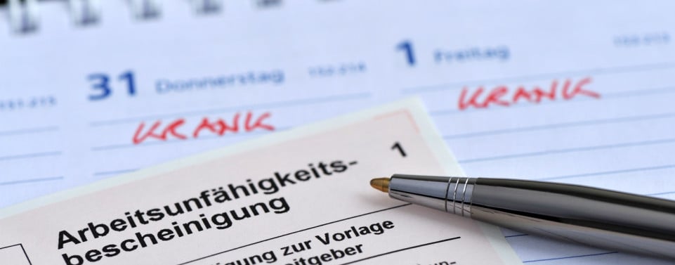 Arbeitsunfähigkeitsbescheinigung mit Stift liegen auf einem Kalender.