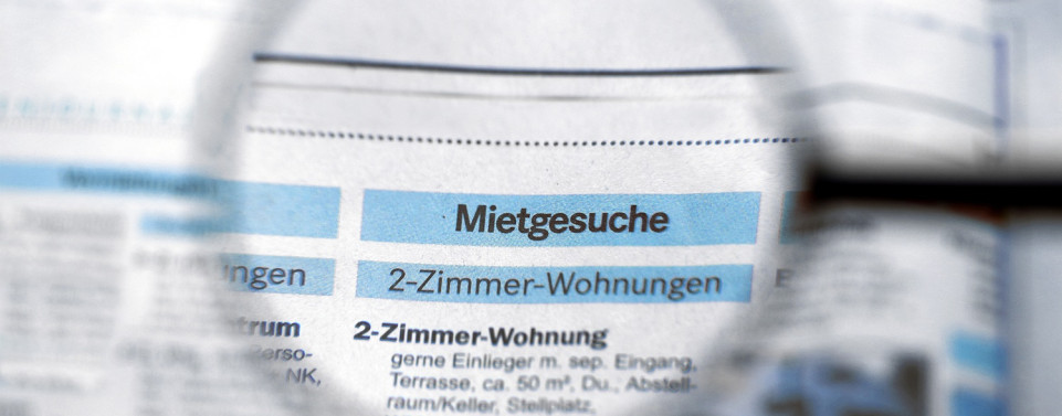 Zeitungsseite mit dem Titel "Mietgesuche", der durch eine Lupe vergrößert wird. 