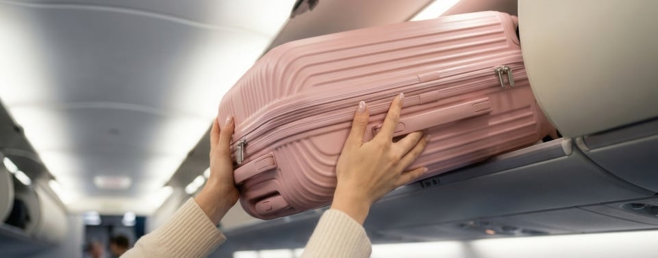 Frau schiebt Handgepäck in die Ablage im Flugzeug.