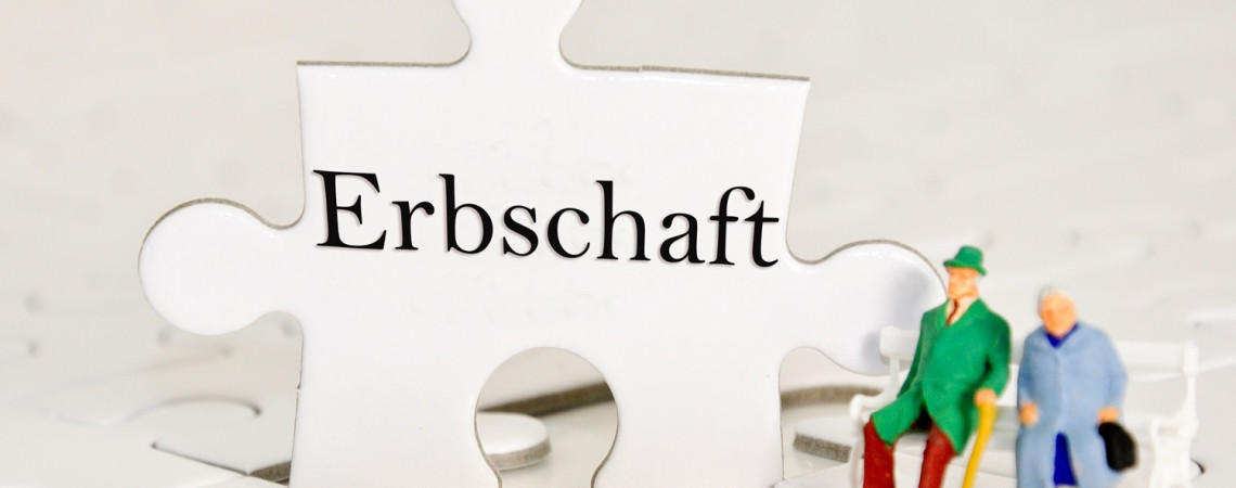 Puzzleteil mit der Aufschrift "Erbschaft" und zwei kleine Figuren, die auf einer kleine kleinen Bank sitzen.