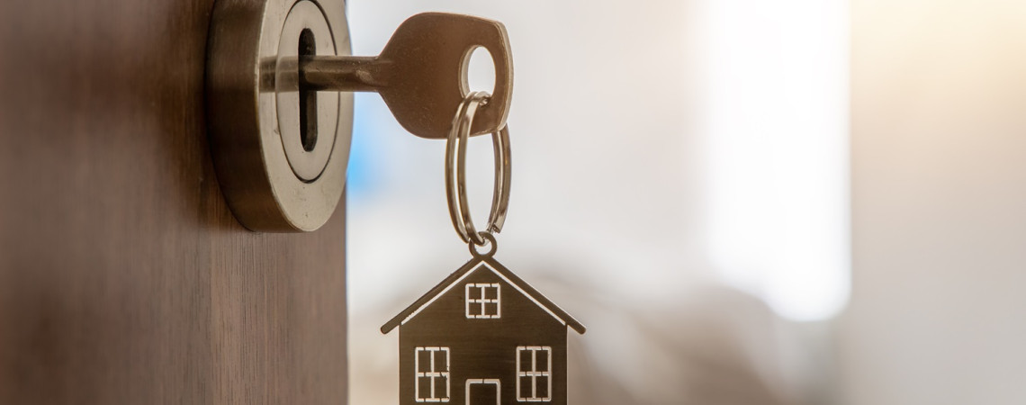 Schlüssel mit einem Schlüsselanhänger, der ein Haus darstellt, steckt im Schlosse einer offen stehenden Tür. Symbolbild für eine Besichtigungsrecht des Vermieters.
