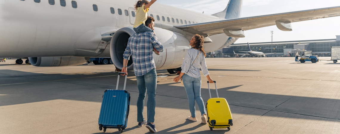 Vater und Mutter mit Tochter gehen auf einem Rollfeld in Richtung Flugzeug. Sie freuen sich.