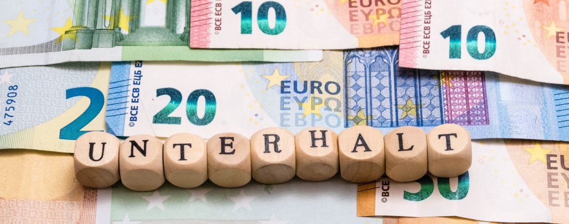 Geldscheine auf denen Holzwürfel liegen. Auf den Würfeln steht Buchstabe für Buchstabe "Unterhalt"