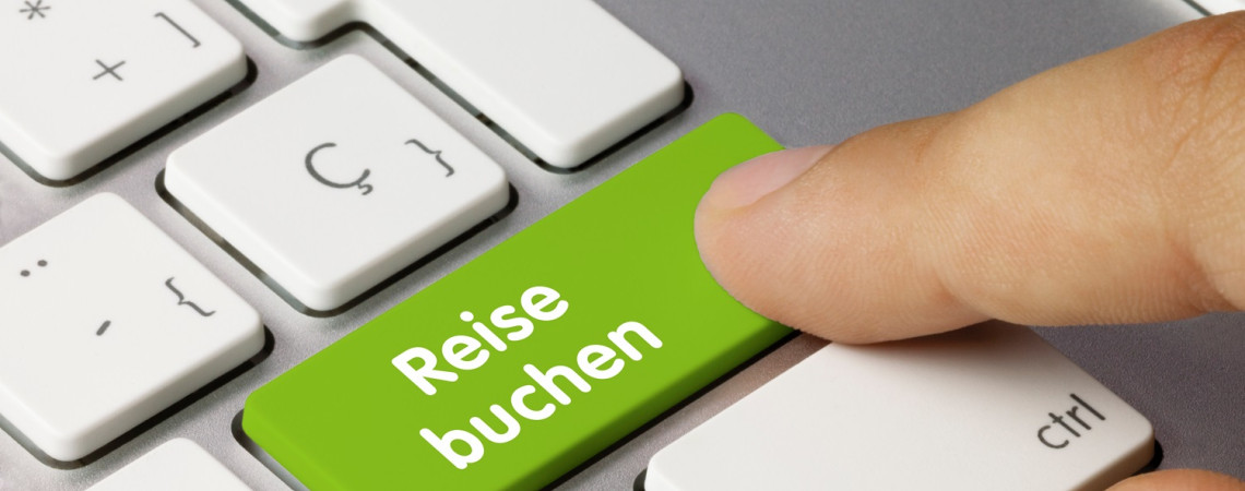 Symbolbild für Vertragsschluss im Internet. Eine Tastatur und auf einer Taste steht "Reise buchen" darüber liegt ein Finger.