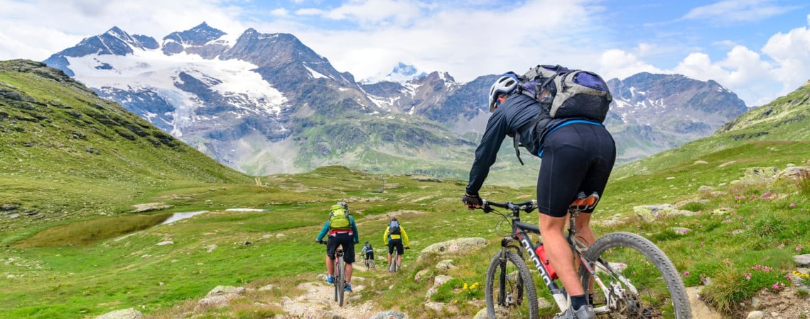 Gruppe von Mountainbiker fahren in einen unebenen Pfad in einer Berglandschaft hinunter.