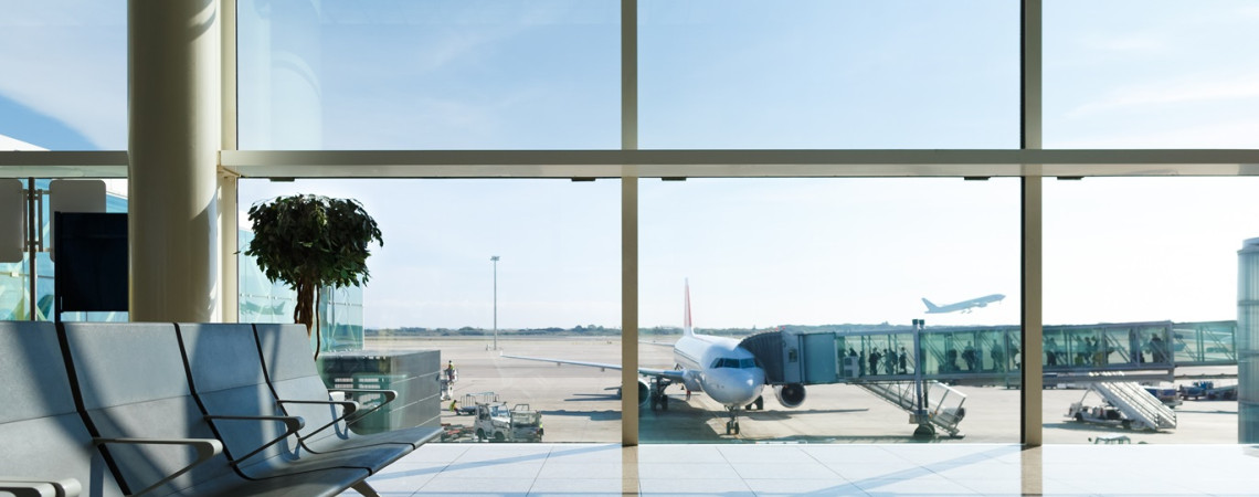 Sicht aus einem Flughafenfenster auf das Rollfeld, wo ein Flugzeug steht und Passagiere einsteigen.