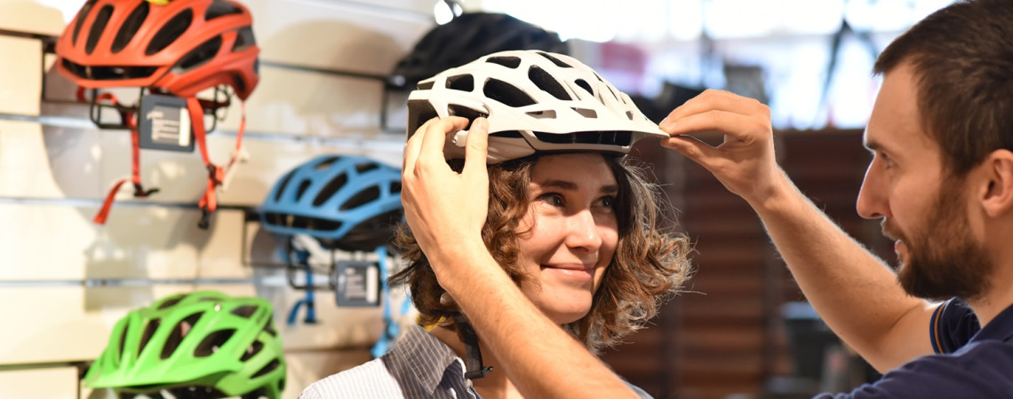 Frau im einen Geschäft probiert einen Fahrradhelm an.