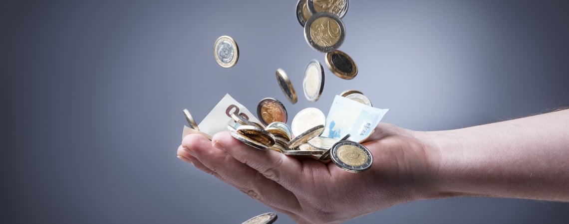 Ausgestreckte Hand fängt Scheine und Münzen, die von oben herabfallen