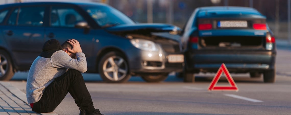 Autounfall und Mann sitzt am Straßenrand