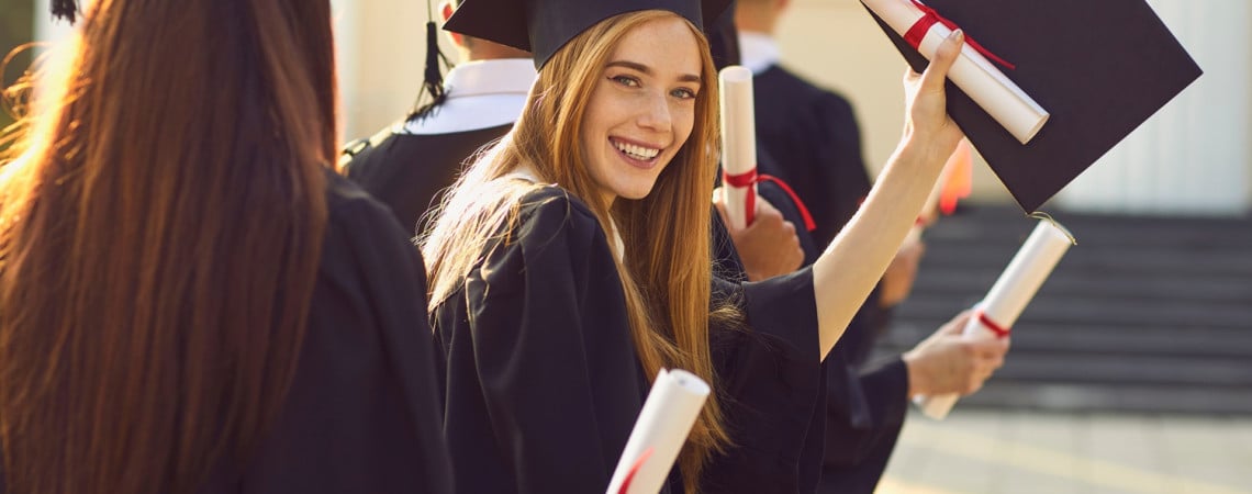 Glückliche Universitiätsabsolventin hält Hut und Diplom in der Hand. 