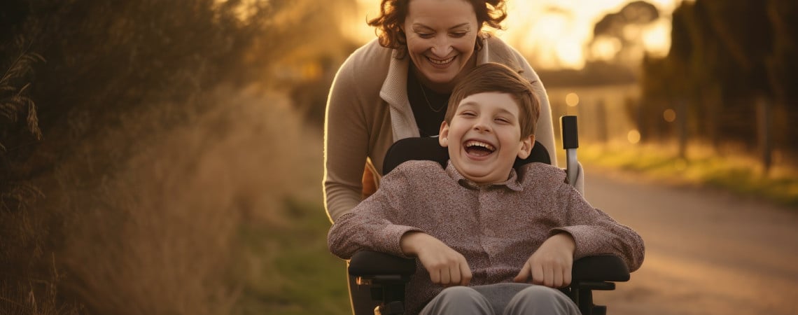 Kind mit Behinderung im Rollstuhl lacht mit Frau.