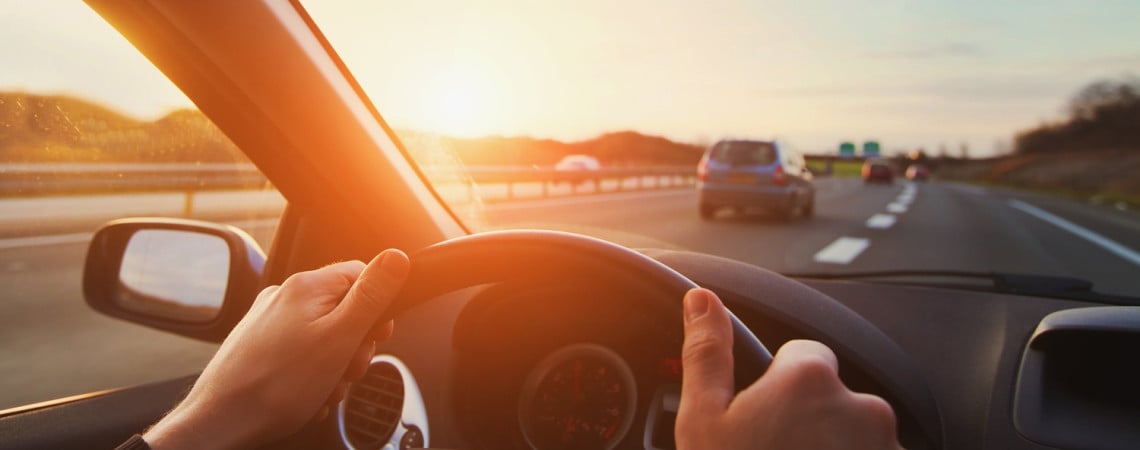 Hände am Steuer eines Autos auf der Straße im Sonnenuntergang. 