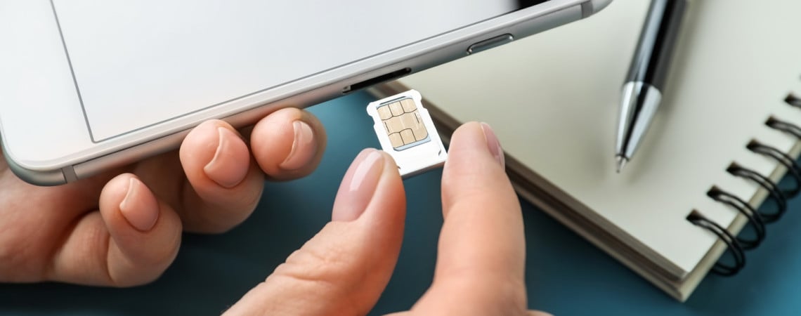 Hände stecken eine Sim-Karte in ein Smartphone.