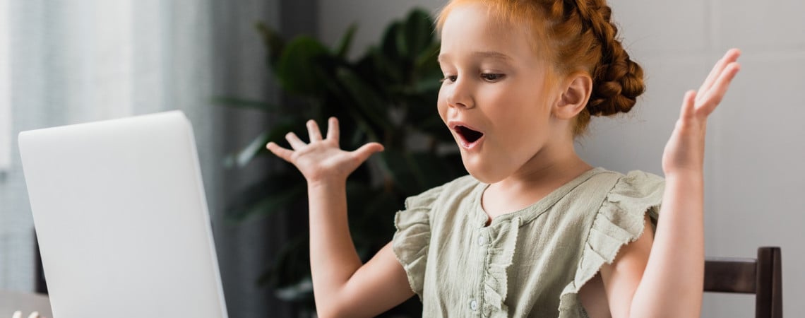 Kleines Mädchen sitzt vor einem Laptop und freut sich.