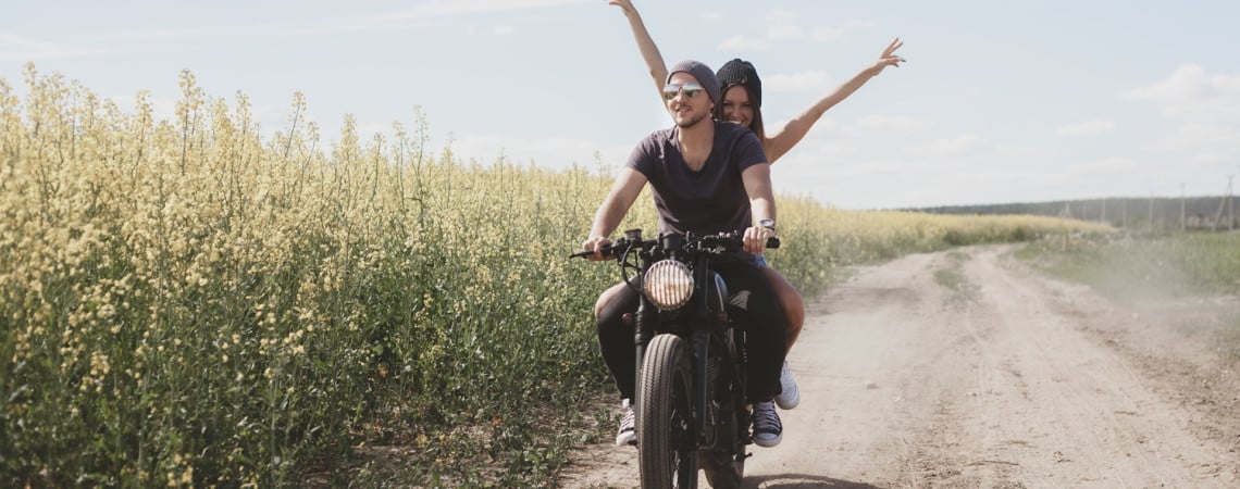 Lachendes Paar auf dem Motorrad auf Feldweg.