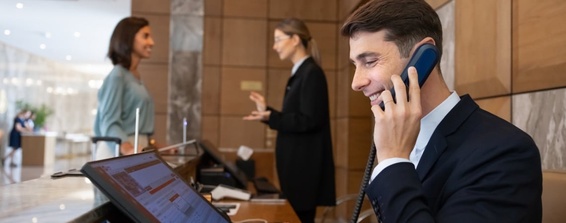 Man an Hotelrezeption am Telefon und Computer.