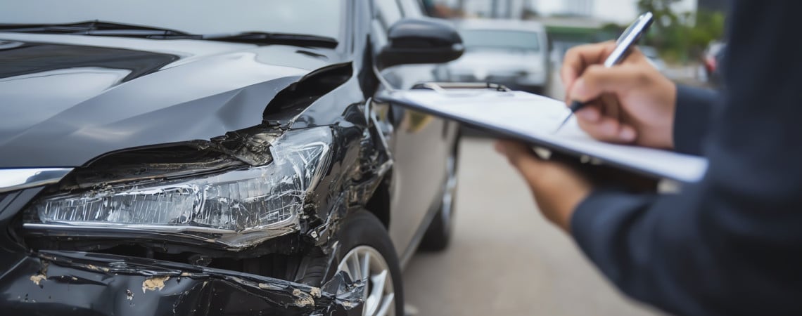Auto nach einem Unfall beschädigt und Person mit Klemmbrett macht Notizen.
