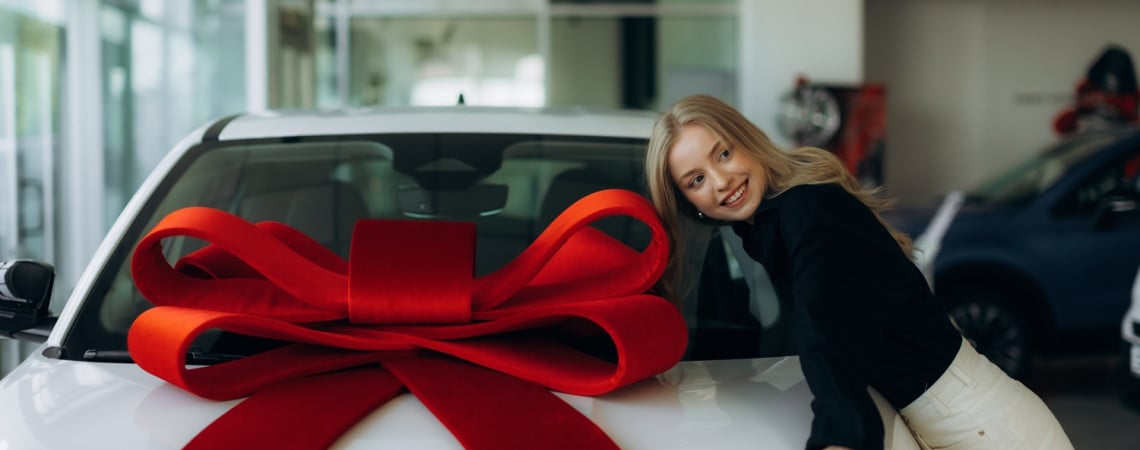Auto mit großer Schleife und glückliche Frau, die sich gegen das Auto lehnt.