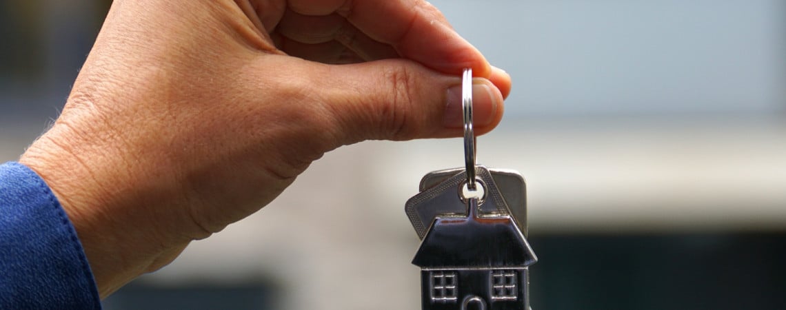 Hand hält Schlüsselbund mit Schlüsselanhänger in Haus-Form. Schlüsselübergabe für die Wohnungsübergabe.