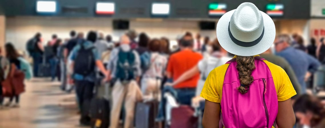 Frau mit Rucksack und Hut steht am Flughafen in der Warteschlange zum Check-in. 
