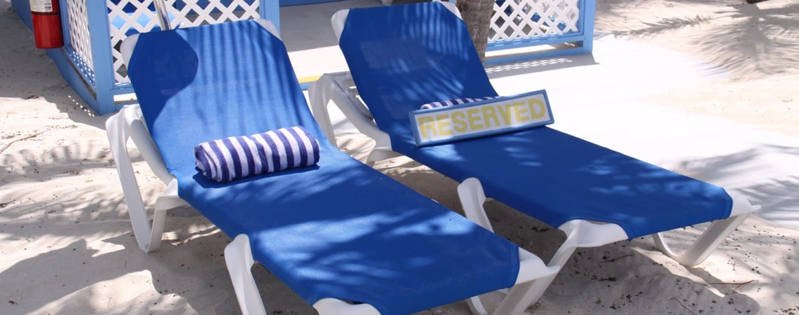 Liegenreservierung. Zwei liegen mit Handtüchern und einem Schild mit "Reserved" am Strand.