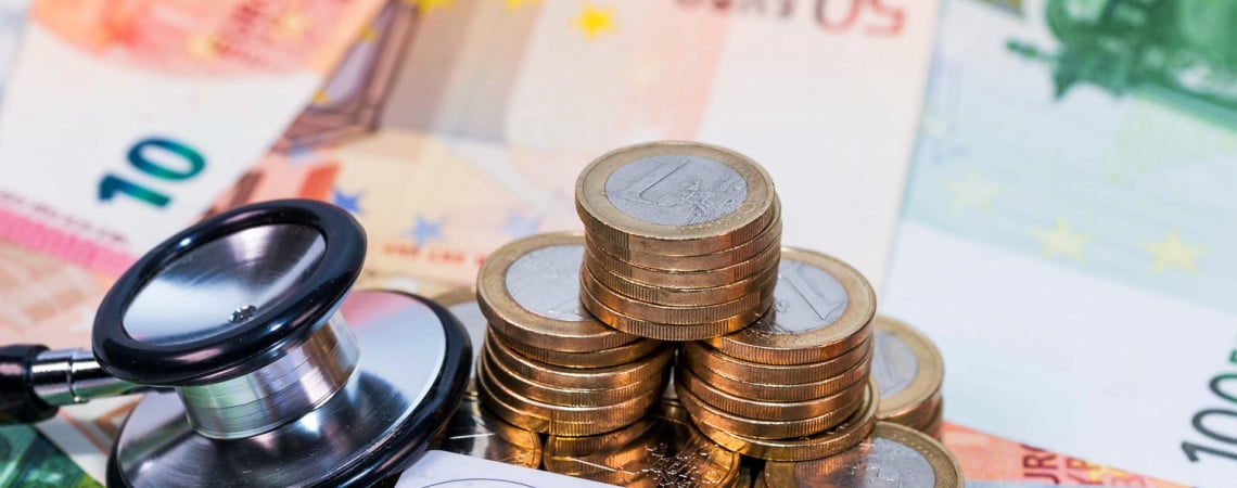 Krankenkassenkarte, Stethoskop und ein mehrere Münzen liegen auf Eurogeldscheinen.