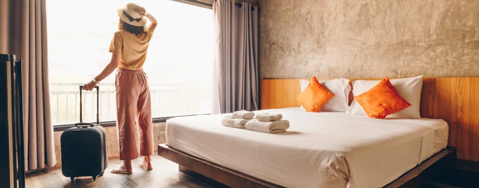 Frau steht mit Koffer in einem Hotelzimmer