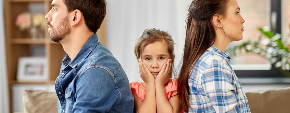 Eltern sitzen mit Kind auf dem Sofa. Kind ist unglücklich und sitzt in der Mitte. Eltern drehen sich den Rücken zu.