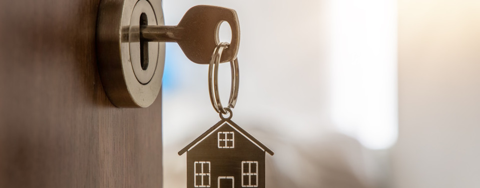 Schlüssel mit einem Schlüsselanhänger, der ein Haus darstellt, steckt im Schlosse einer offen stehenden Tür. Symbolbild für eine Besichtigungsrecht des Vermieters.