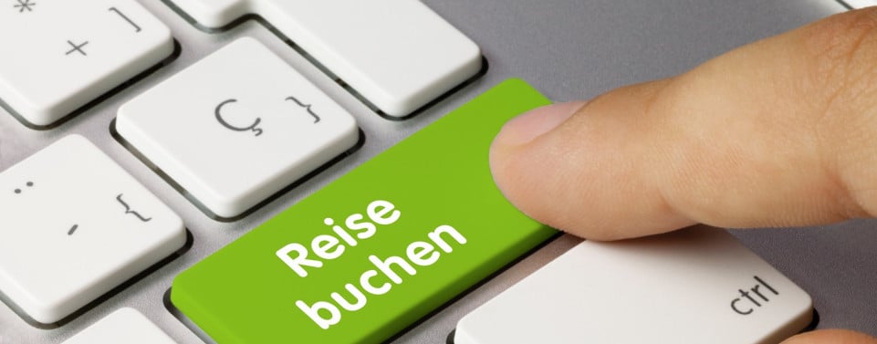 Symbolbild für Vertragsschluss im Internet. Eine Tastatur und auf einer Taste steht "Reise buchen" darüber liegt ein Finger.