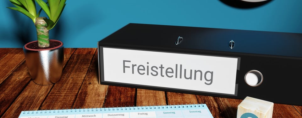 Ordner mit Aufschrift "Freistellung" liegt auf einem Tisch. Ein Kalender mit und ein Würfel mit deinem Paragrafen-Zeichen liegen auf dem Tisch. 
