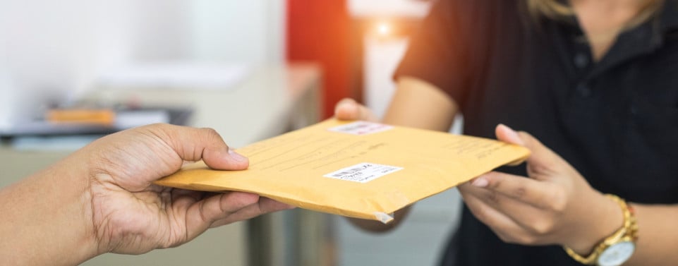 Eine Hand übergibt einen braunen Brief an eine Frau.
