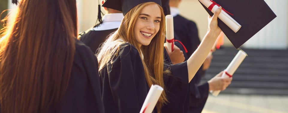 Glückliche Universitiätsabsolventin hält Hut und Diplom in der Hand. 