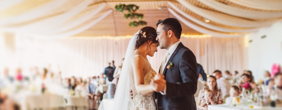 Hochzeitsfoto mit Brautpaar beim Tanzen und Gäste im Hintergrund.