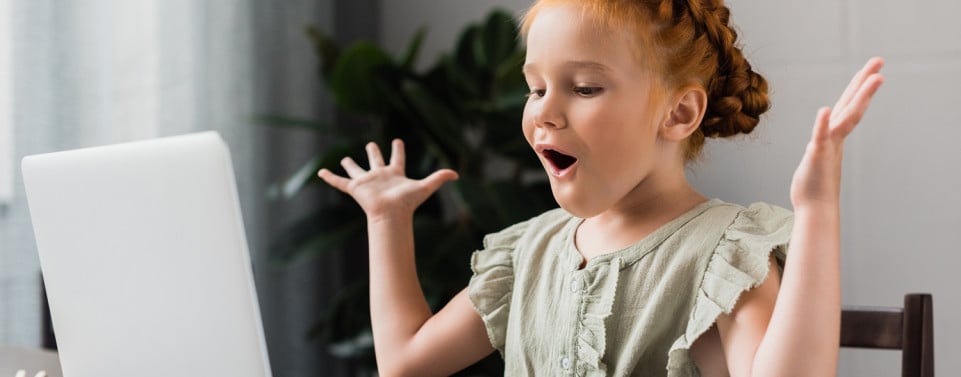 Kleines Mädchen sitzt vor einem Laptop und freut sich.
