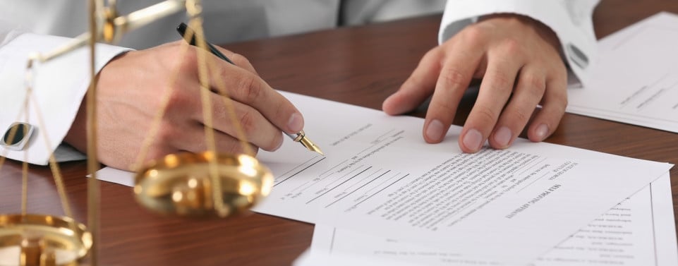 Mann unterschreibt ein Testament. Im Vordergrund steht eine goldene Waage.
