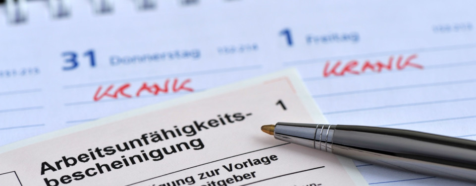 Arbeitsunfähigkeitsbescheinigung mit Stift liegen auf einem Kalender.