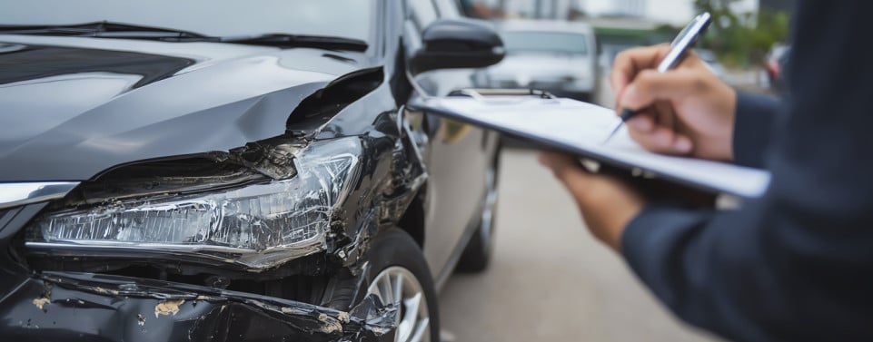 Auto nach einem Unfall beschädigt und Person mit Klemmbrett macht Notizen.