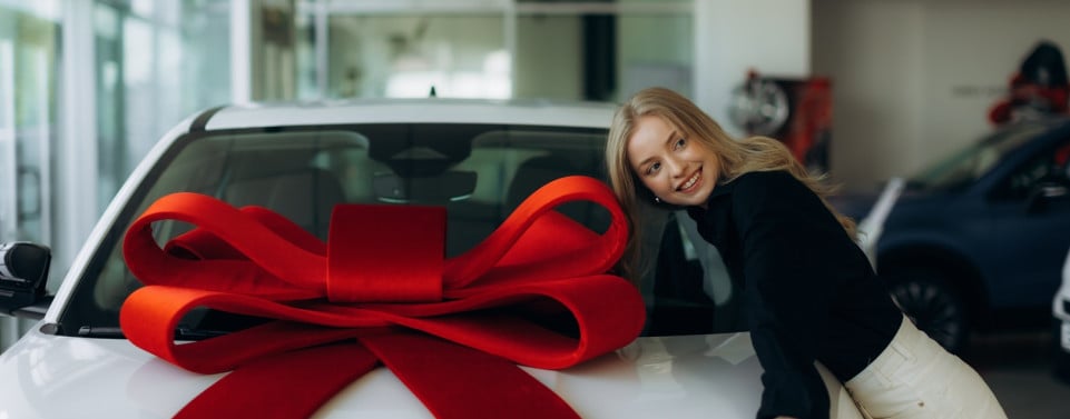 Auto mit großer Schleife und glückliche Frau, die sich gegen das Auto lehnt.