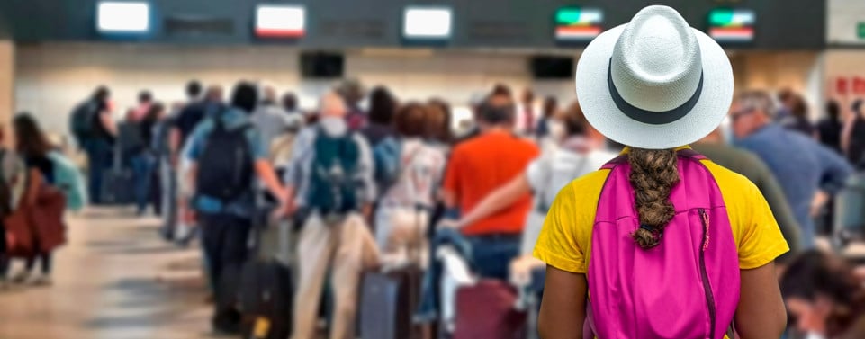 Frau mit Rucksack und Hut steht am Flughafen in der Warteschlange zum Check-in. 